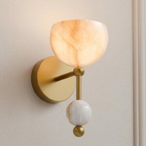 Wall-mounted light fixture with a gold arm and marble-like shade on a neutral background