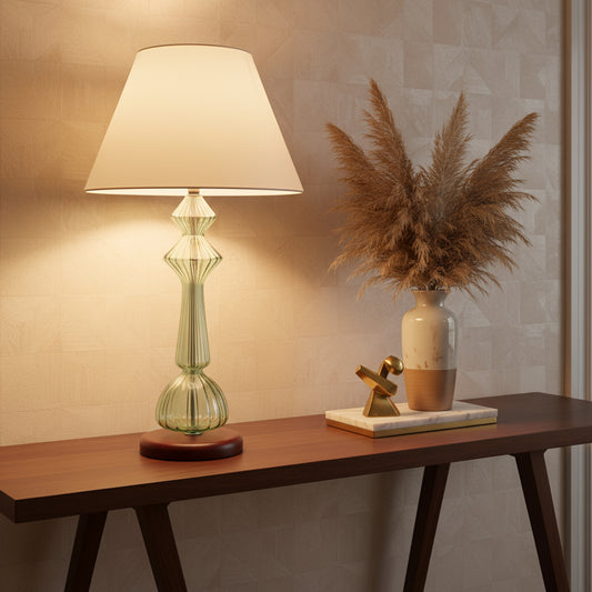 Decorative table lamp with a white shade and green glass base against a textured wall | Les Trois Pyramides