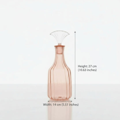 Pink glass decanter with a wine glass and flowers on a marble surface.