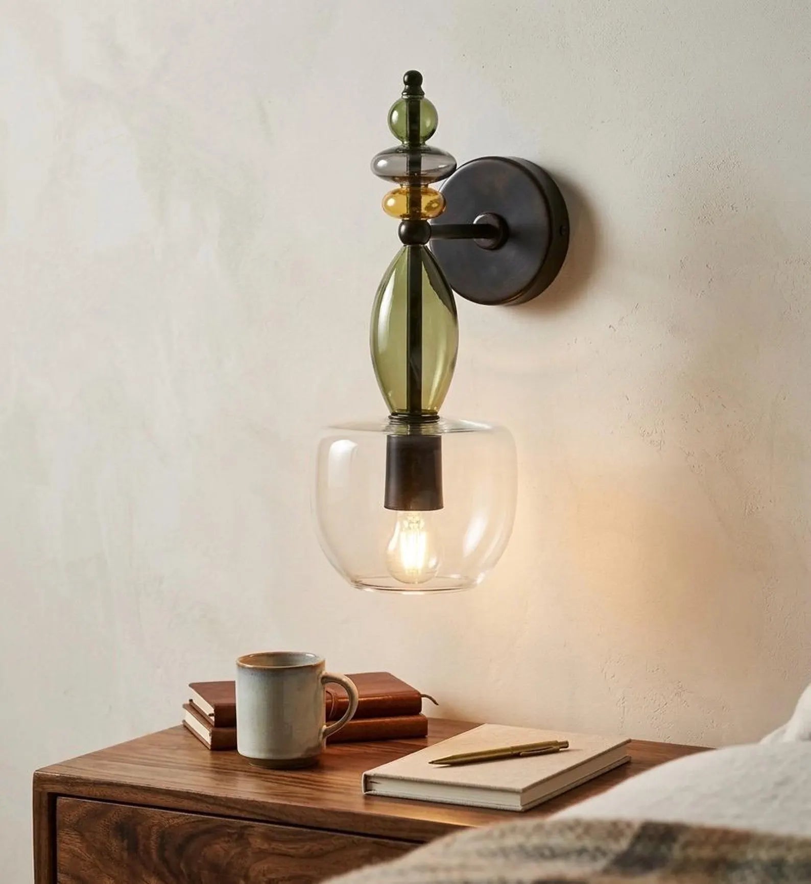 Wall-mounted lamp with glass shade on a wooden surface with books and a mug.