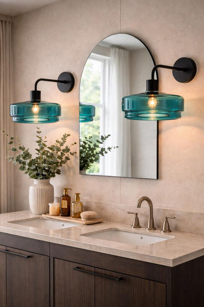 Bathroom vanity with teal glass sconces, mirror, and decorative items.
