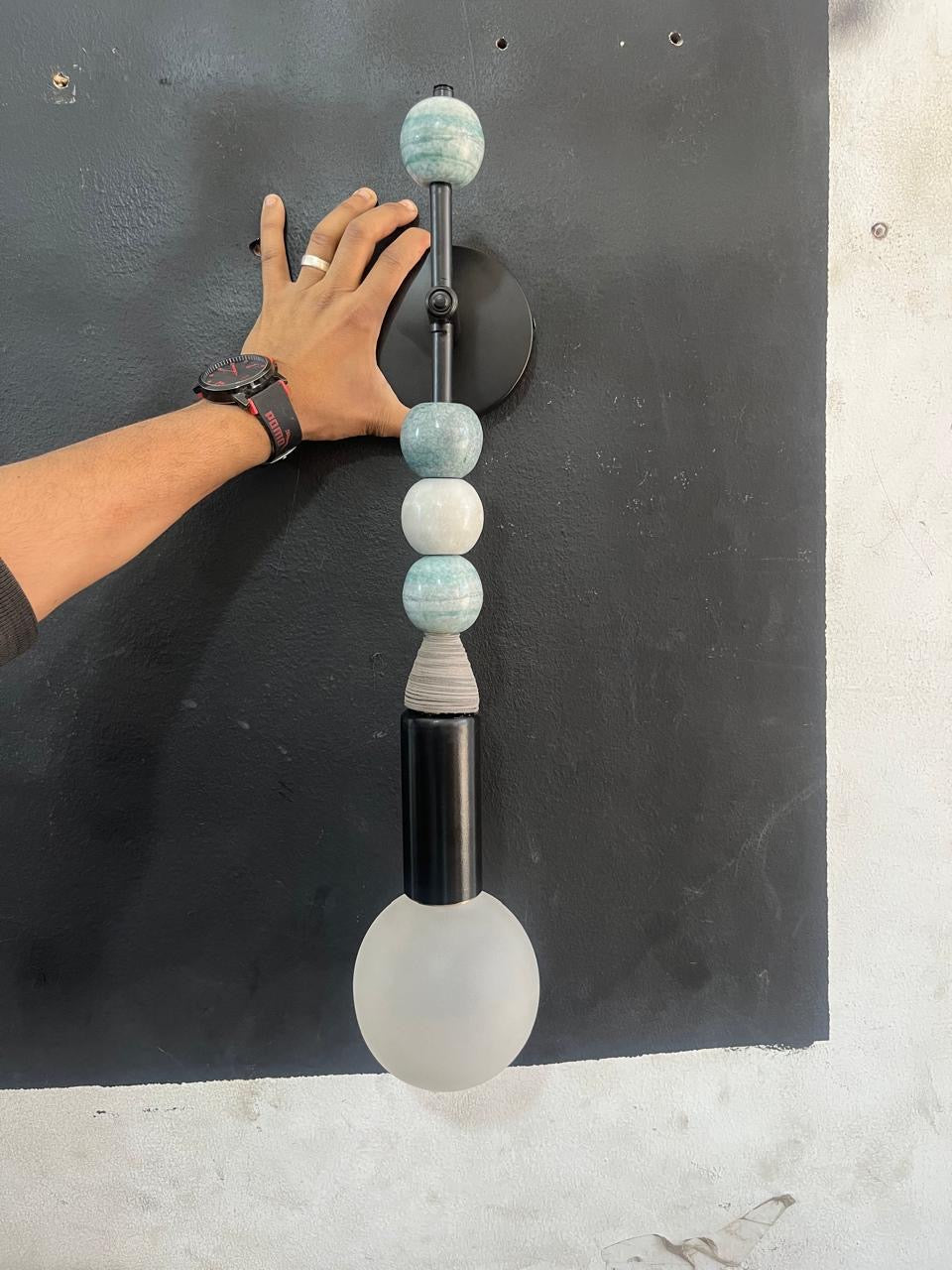 Artisan crafting a handmade wall sconce with natural jade stones and Frosted glass globe in workshop | Les Trois Pyramides