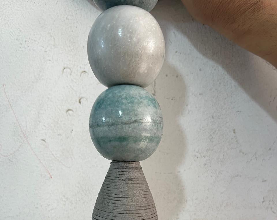 Artisan crafting a handmade wall sconce with natural jade stones and glass globe in workshop | Les Trois Pyramides