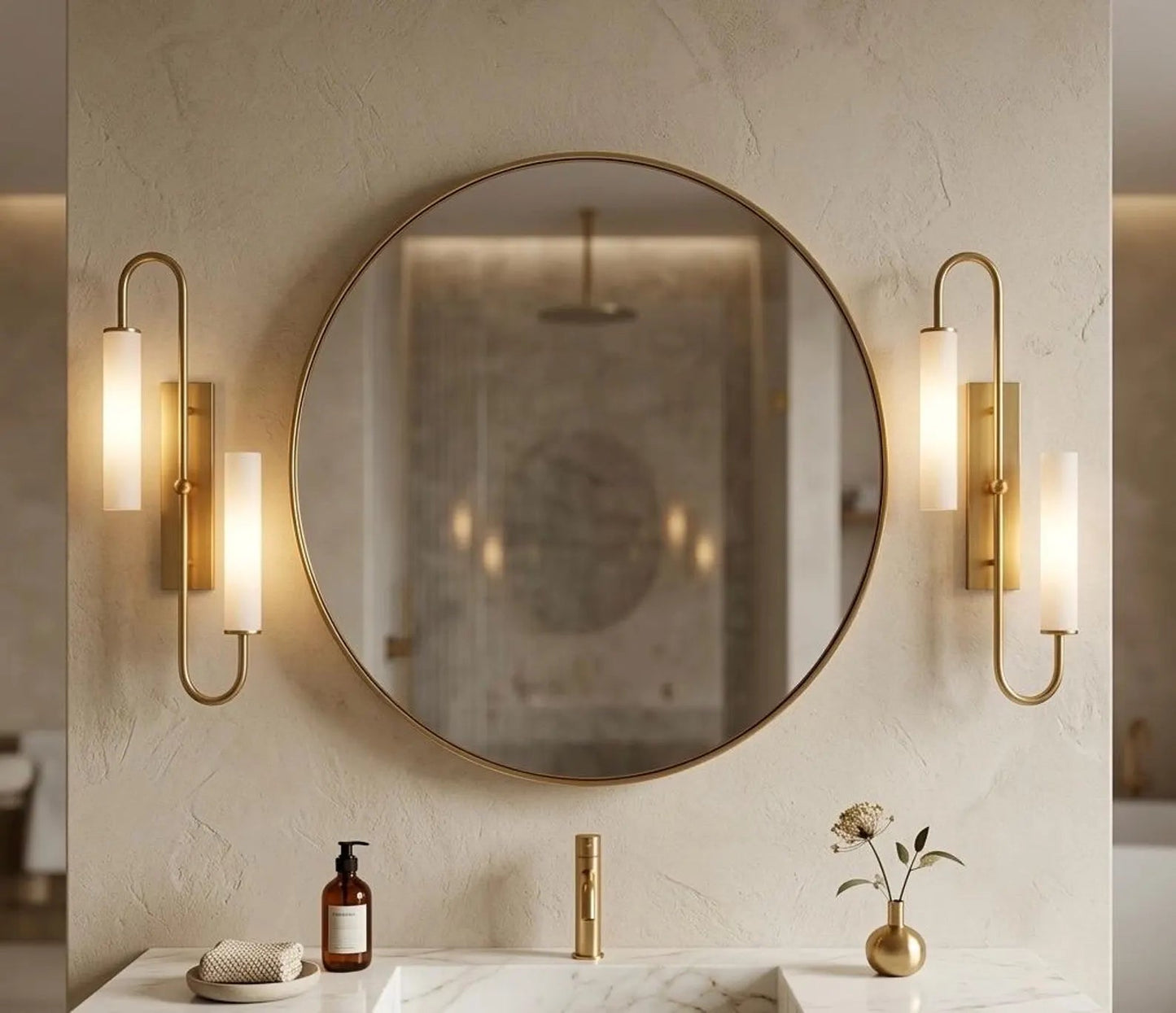 Round mirror with gold frame in a bathroom setting with wall lights and decor.