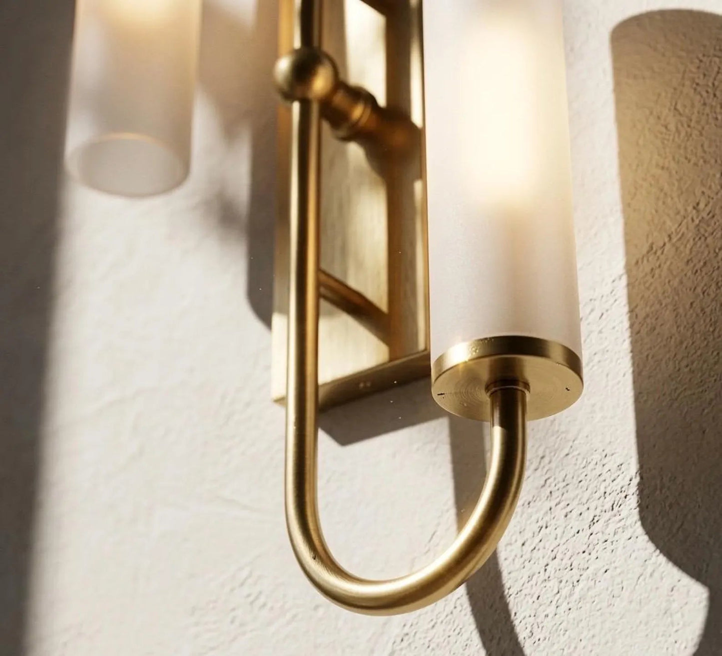 Gold wall sconce with cylindrical glass shades on a textured wall.