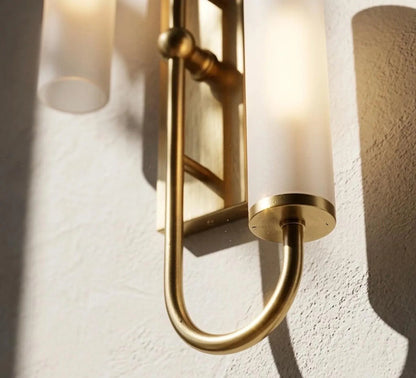 Gold wall sconce with cylindrical glass shades on a textured wall.