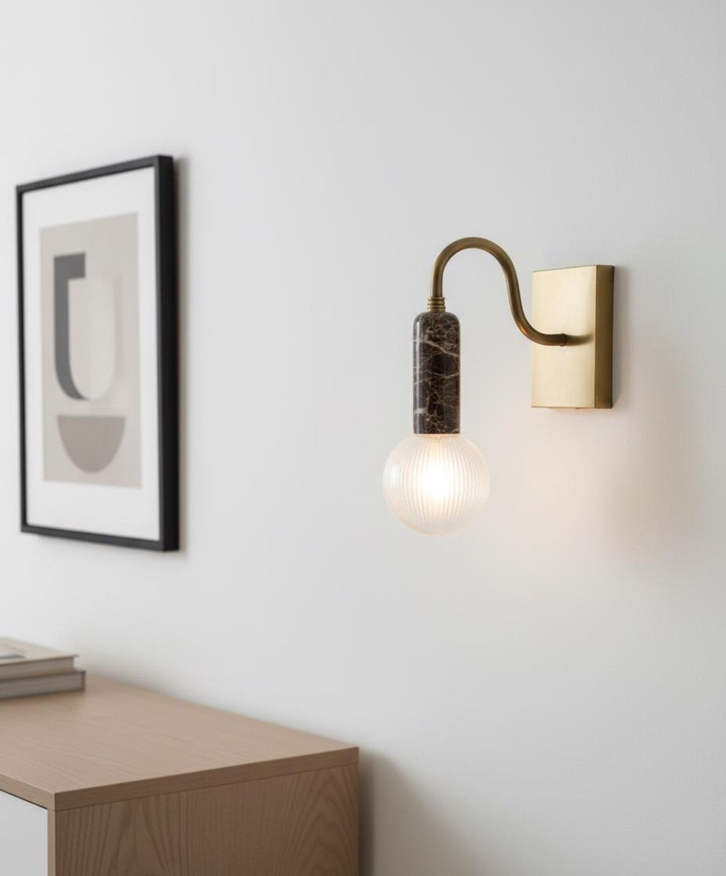 Modern wall sconce with a light bulb on a white wall next to a framed abstract art piece.