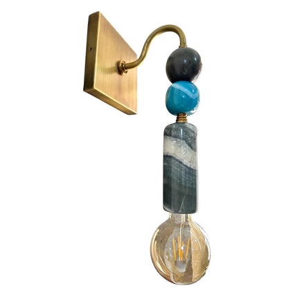 Decorative wall sconce with gold arm, black and blue marble-like beads, and a visible light bulb on a white background.