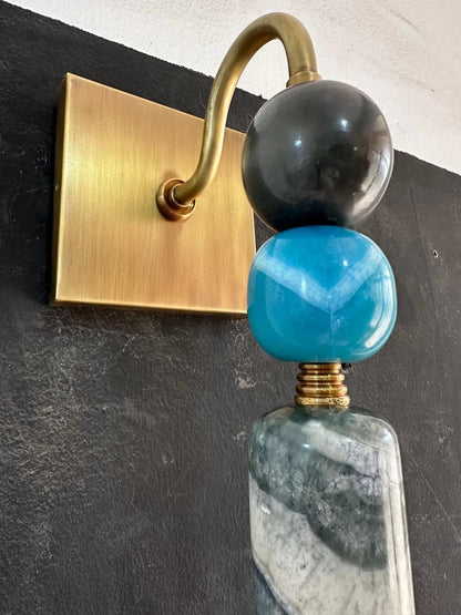 Decorative wall sconce with gold arm, black and blue glass spheres on a dark wall.