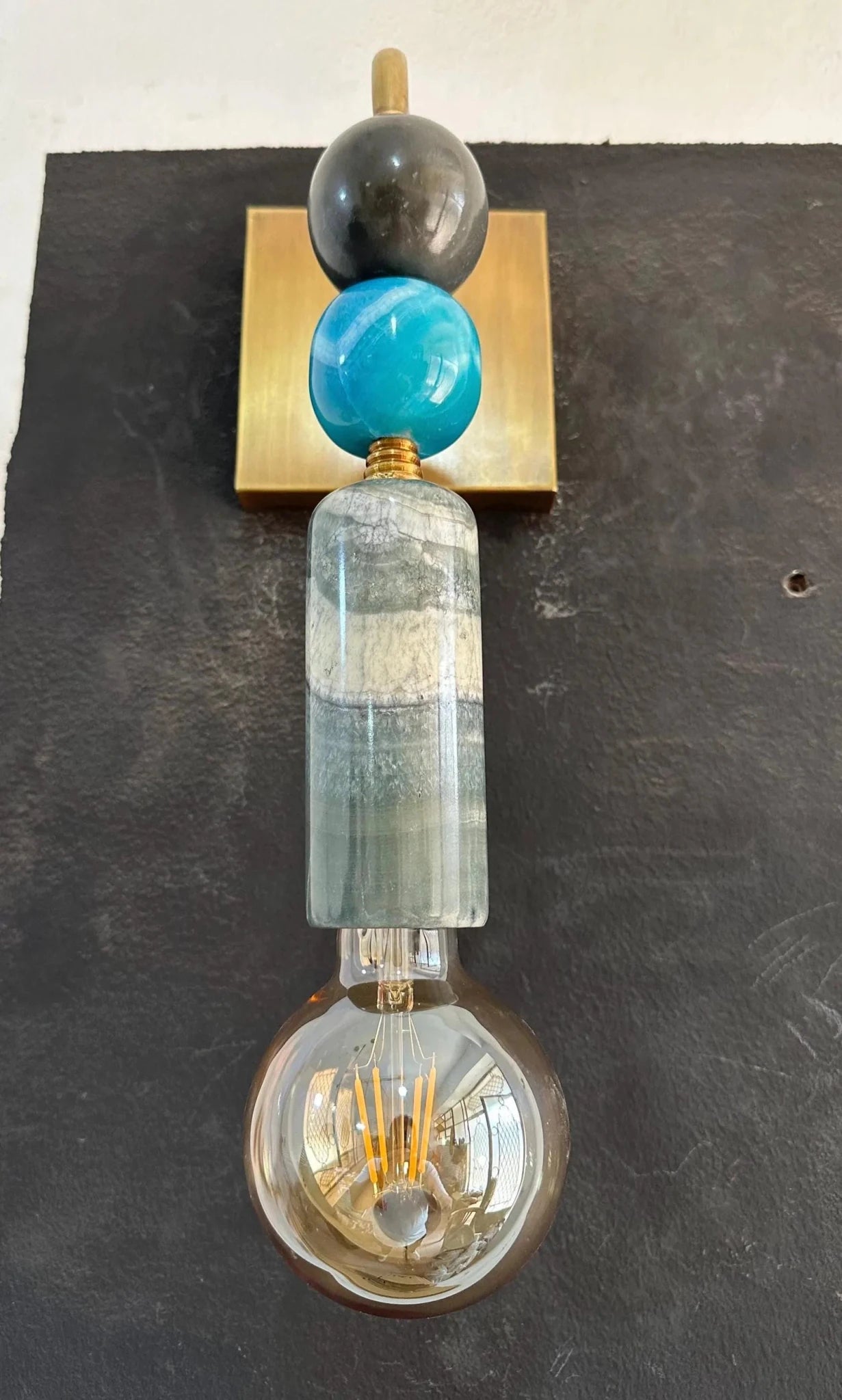 Decorative wall light fixture with a blue glass orb and gold accents on a dark background