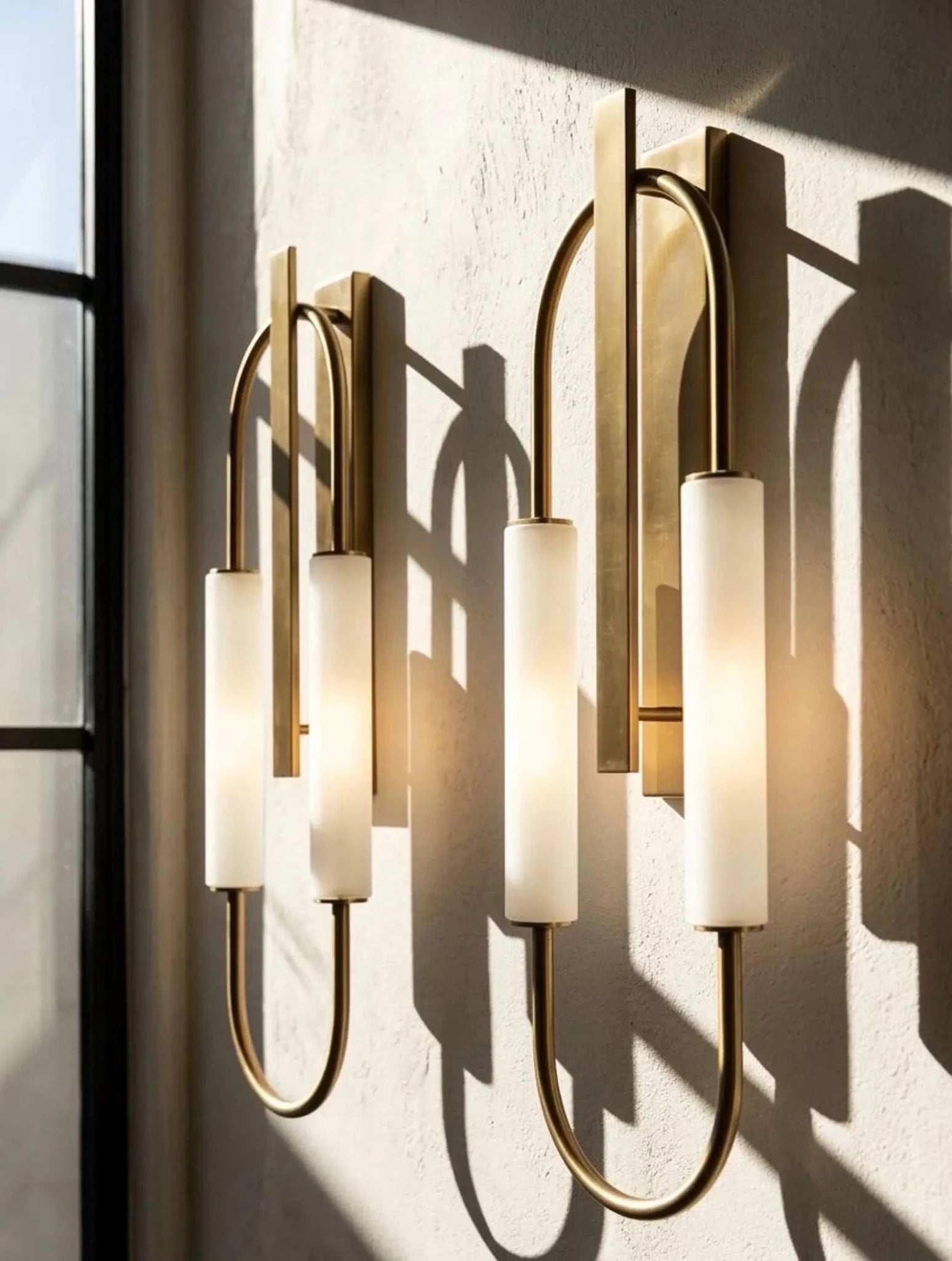 Pair of gold wall sconces with white glass shades on a textured wall.