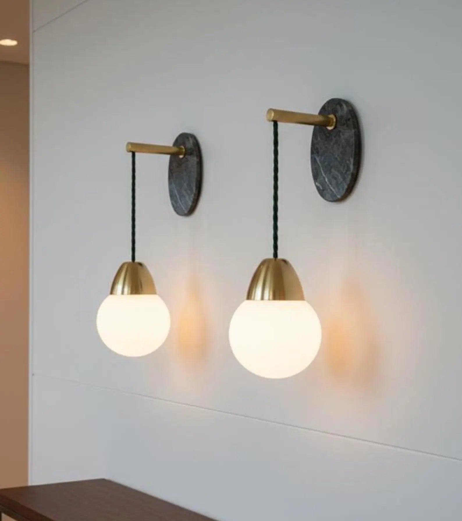 Two wall-mounted lights with gold fixtures and white glass shades on a light gray wall.