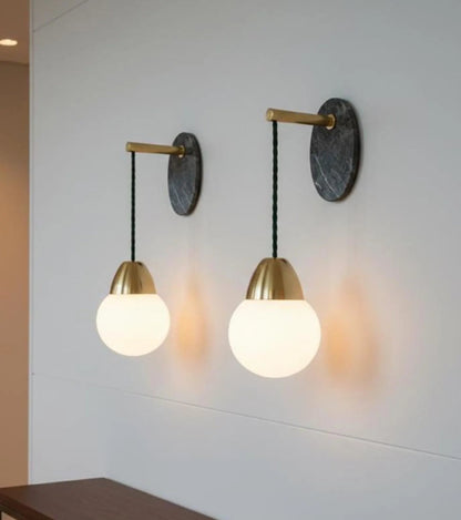 Two wall-mounted lights with gold fixtures and white glass shades on a light gray wall.