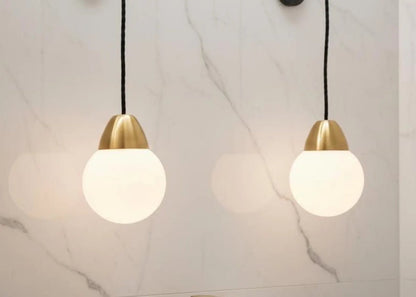 Two pendant lights with gold fixtures and white glass shades on a marble wall background.