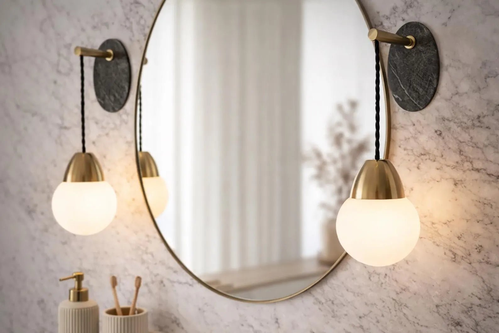 Round mirror with two gold wall lights on a marble wall.