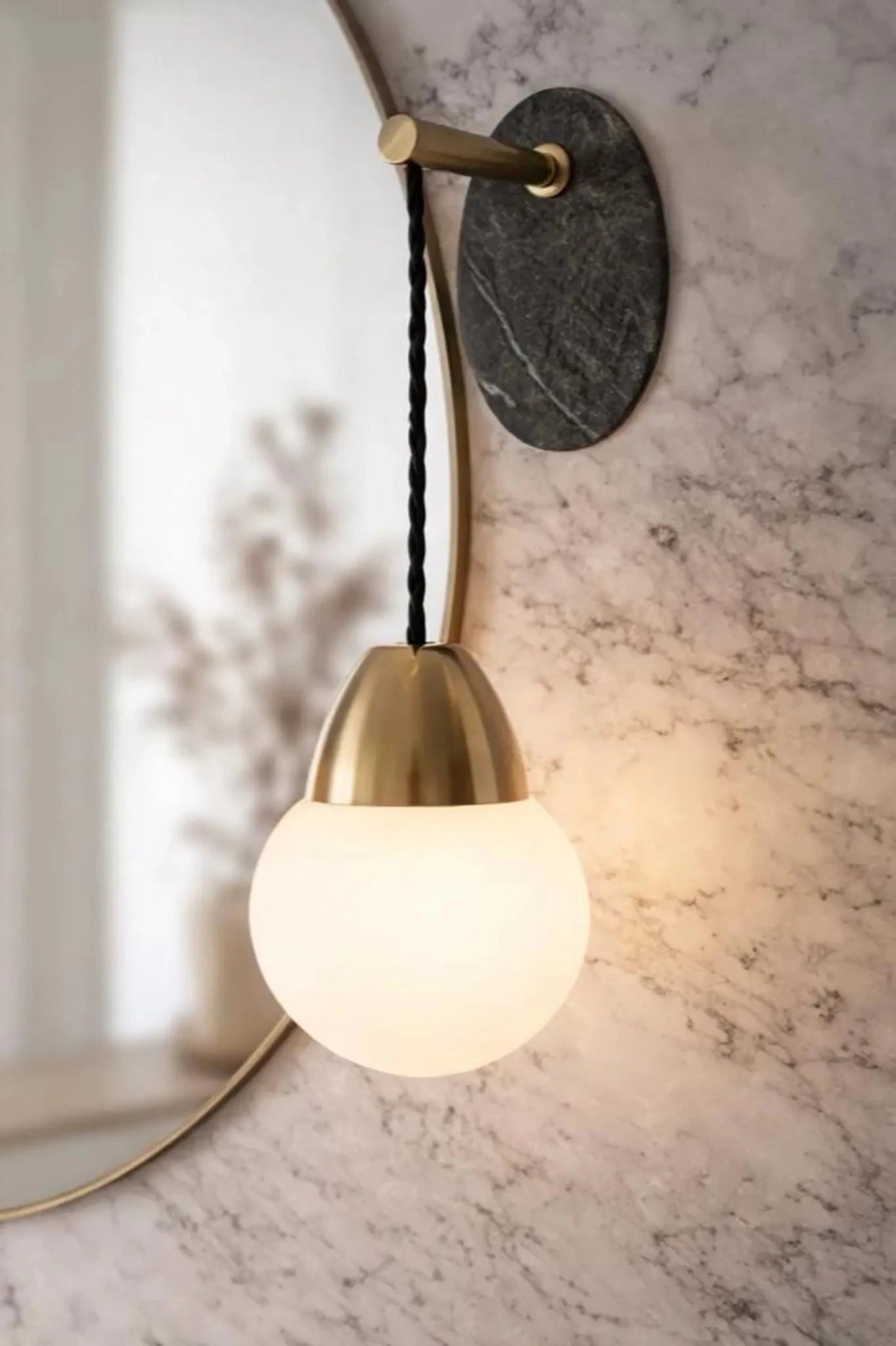 Wall-mounted light fixture with brass finish and glass shade on a marble wall.