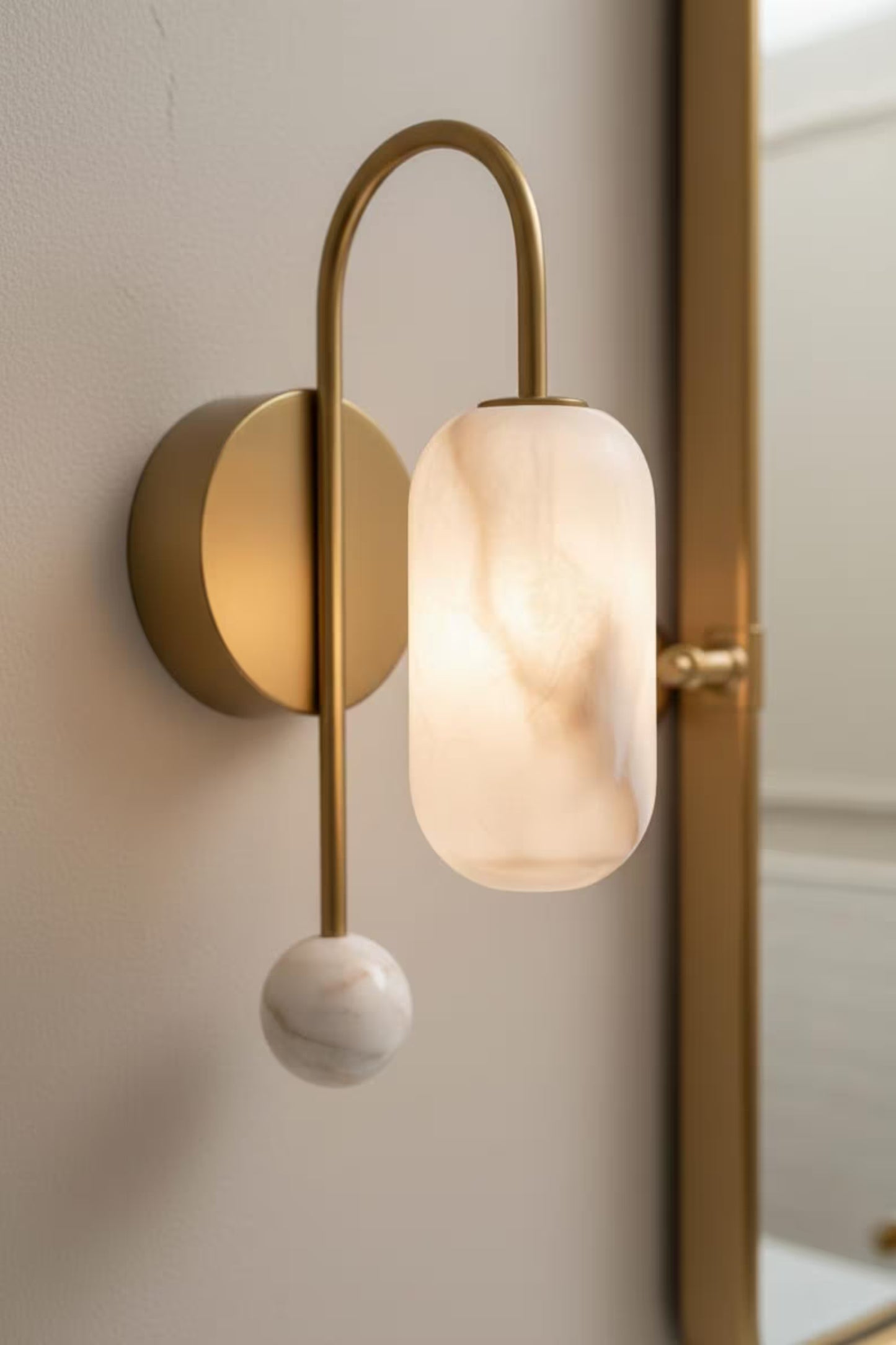 Modern wall lamp with gold fixture and marble-like shade on a neutral wall.