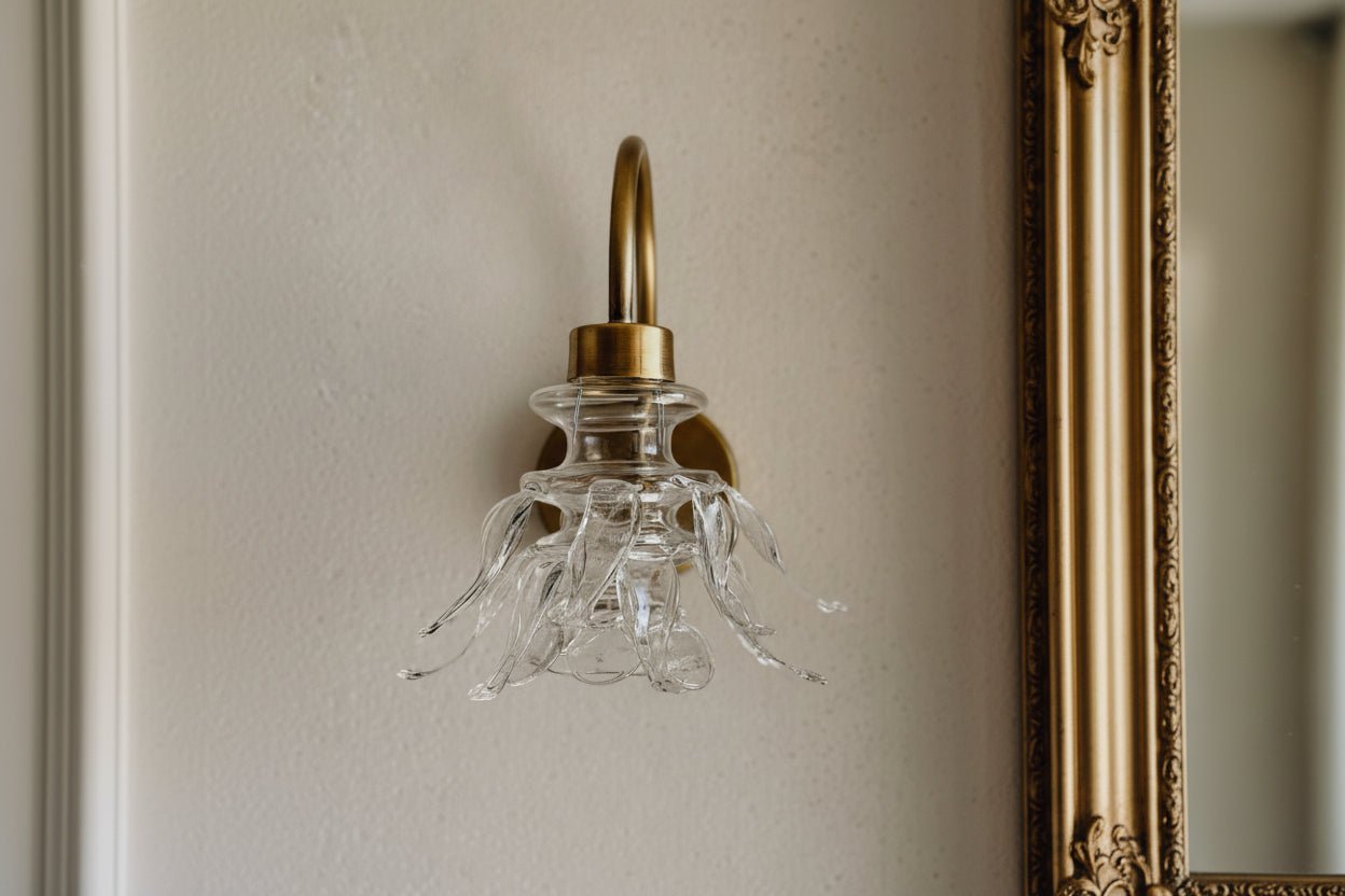 Single upside down bloom wall sconce in hand-formed clear glass with brass arm