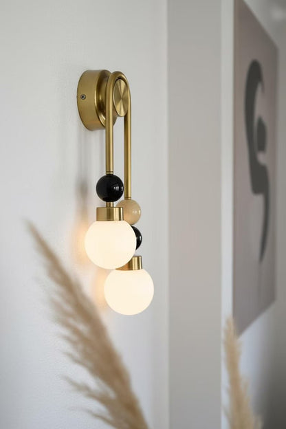 Handmade double brass wall light with natural onyx stone details and frosted glass globes mounted on wall
