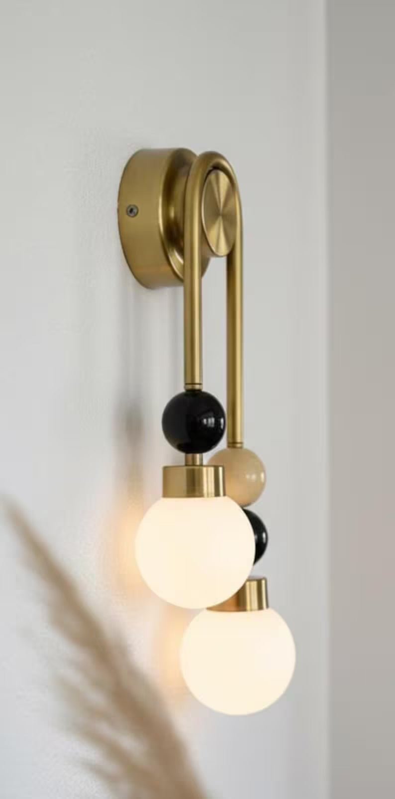 Double brass wall light with onyx stone details installed above bathroom mirror with frosted glass globes side view
