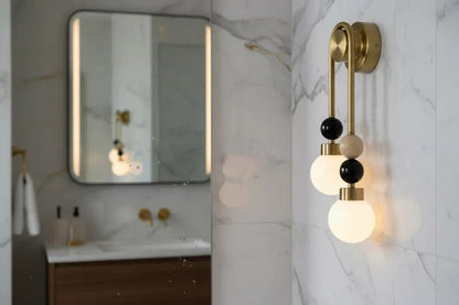 Double brass wall light with onyx stone details installed above bathroom mirror with frosted glass globes
