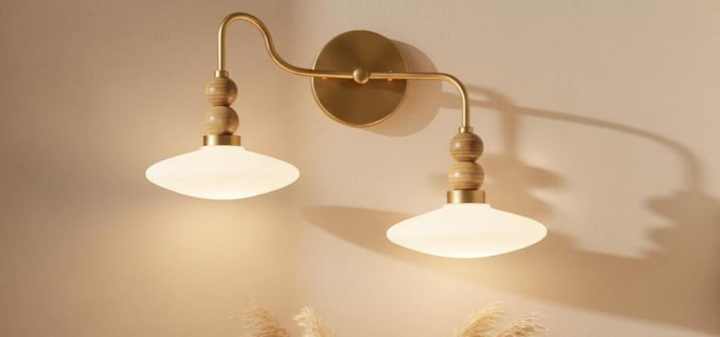 Wall-mounted light fixture with two illuminated lampshades on a beige wall.