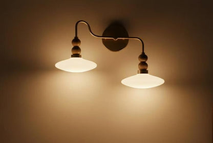 Wall-mounted lamp with two illuminated lampshades on a beige wall.