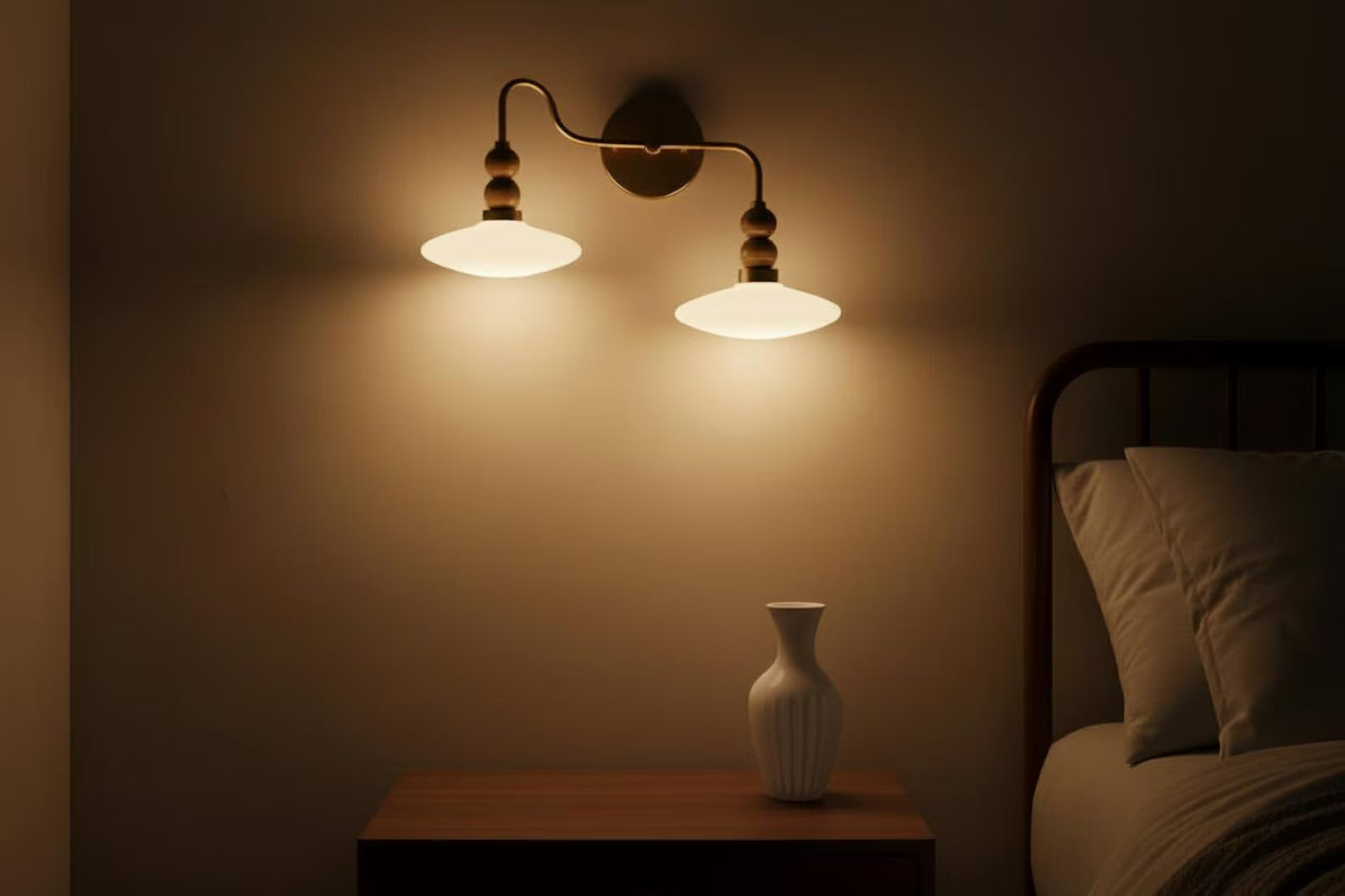 Wall-mounted lamp casting a warm glow in a dimly lit room with a vase on a table.