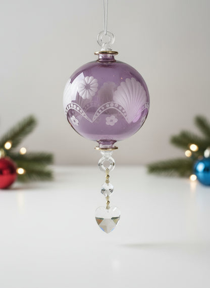 Decorative purple glass ornament with floral patterns hanging on a Christmas tree.