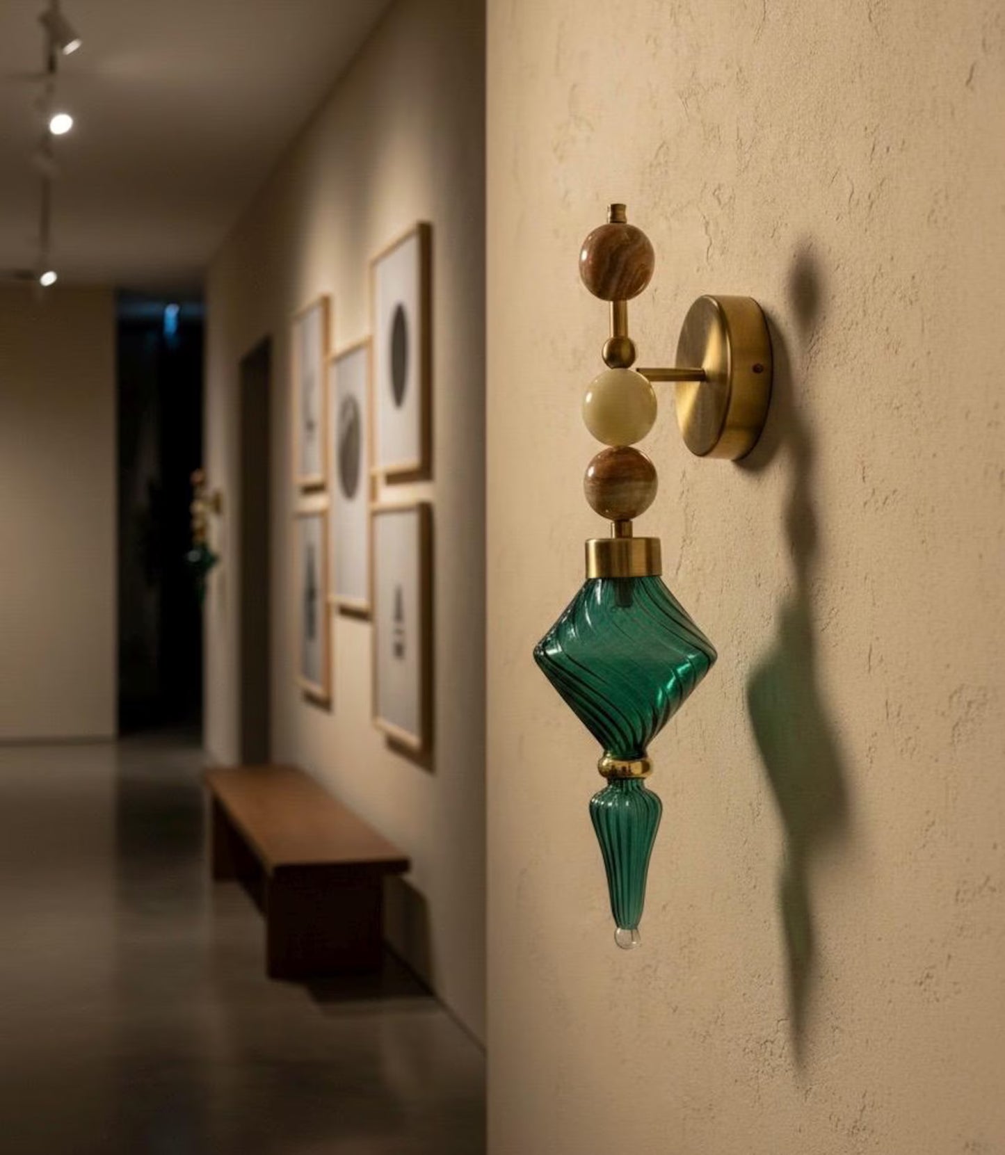 Decorative wall sconce with green glass shade on a beige wall in an art gallery setting.