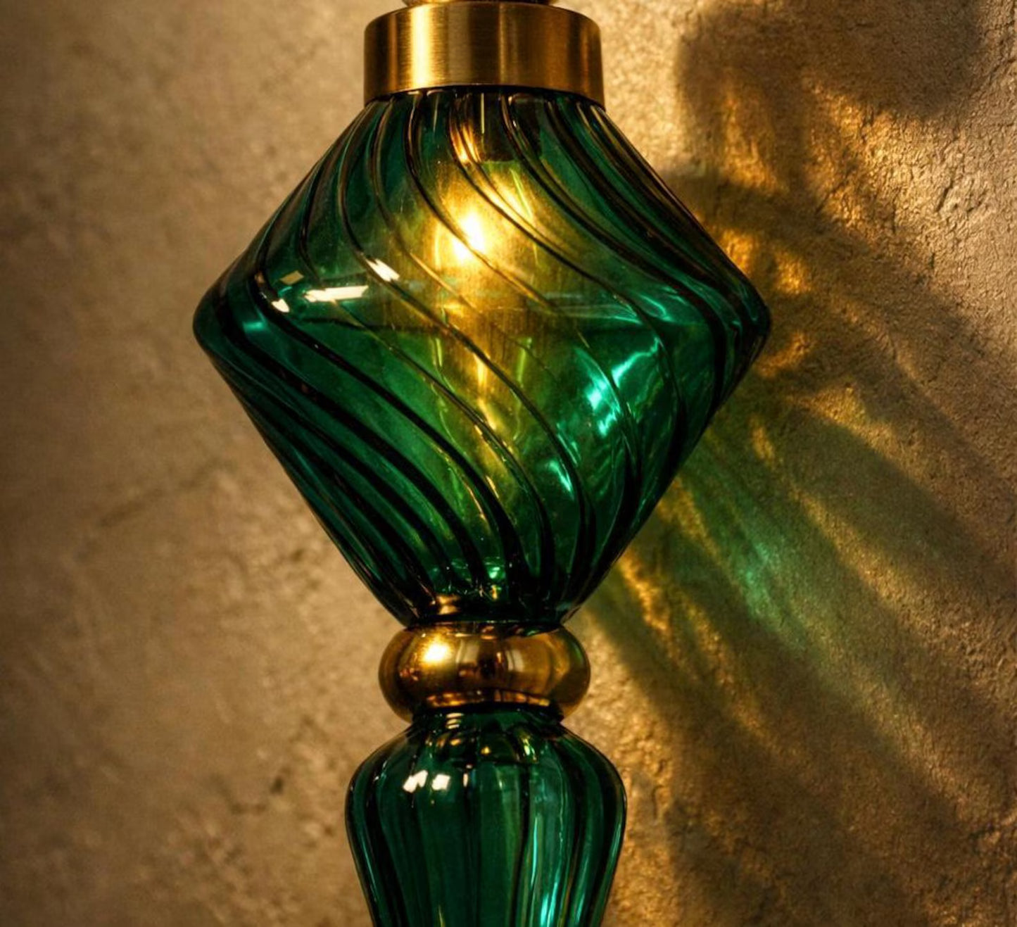 Green glass wall sconce with gold accents casting a shadow on a textured wall.