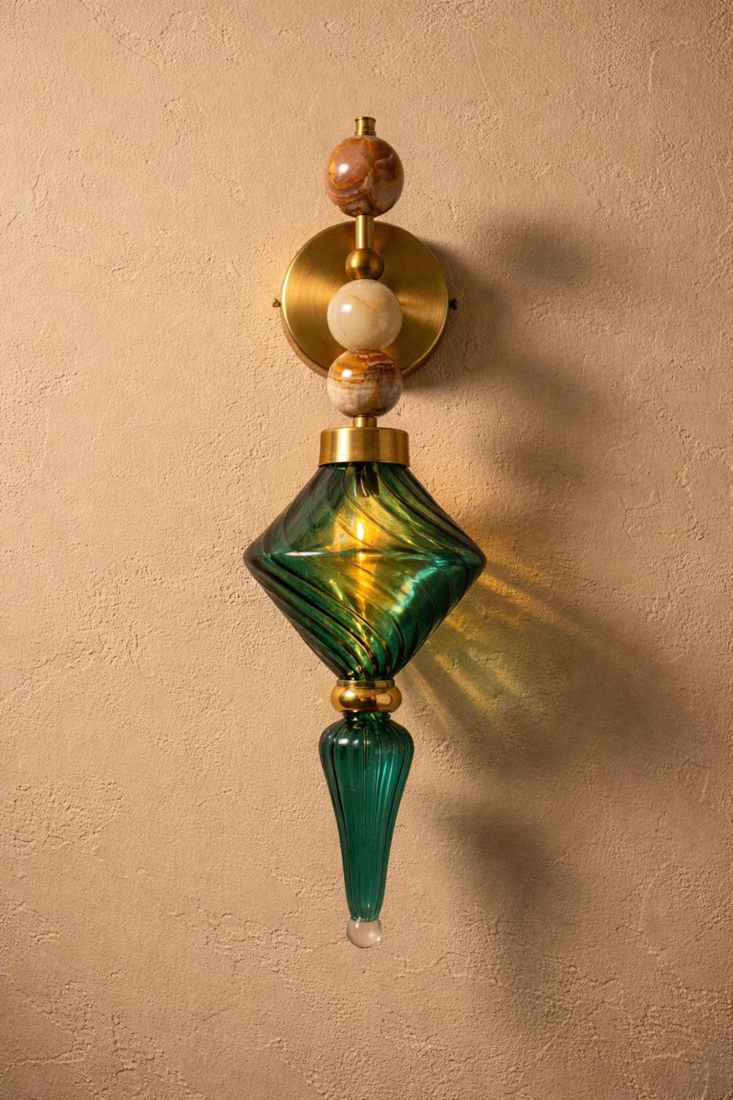 Decorative wall sconce with green glass and gold accents on a beige wall.