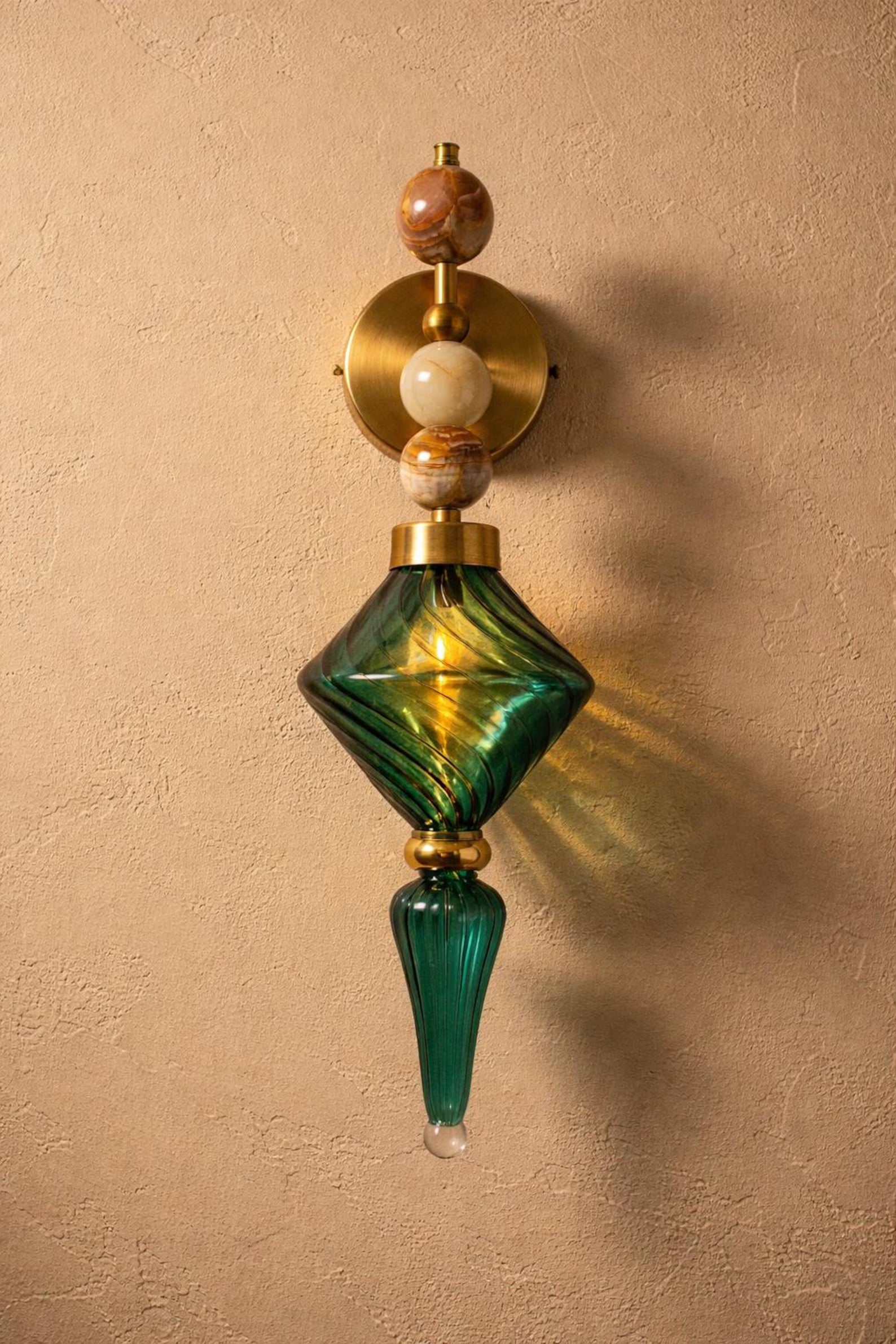 Decorative wall sconce with green glass and gold accents on a beige wall.