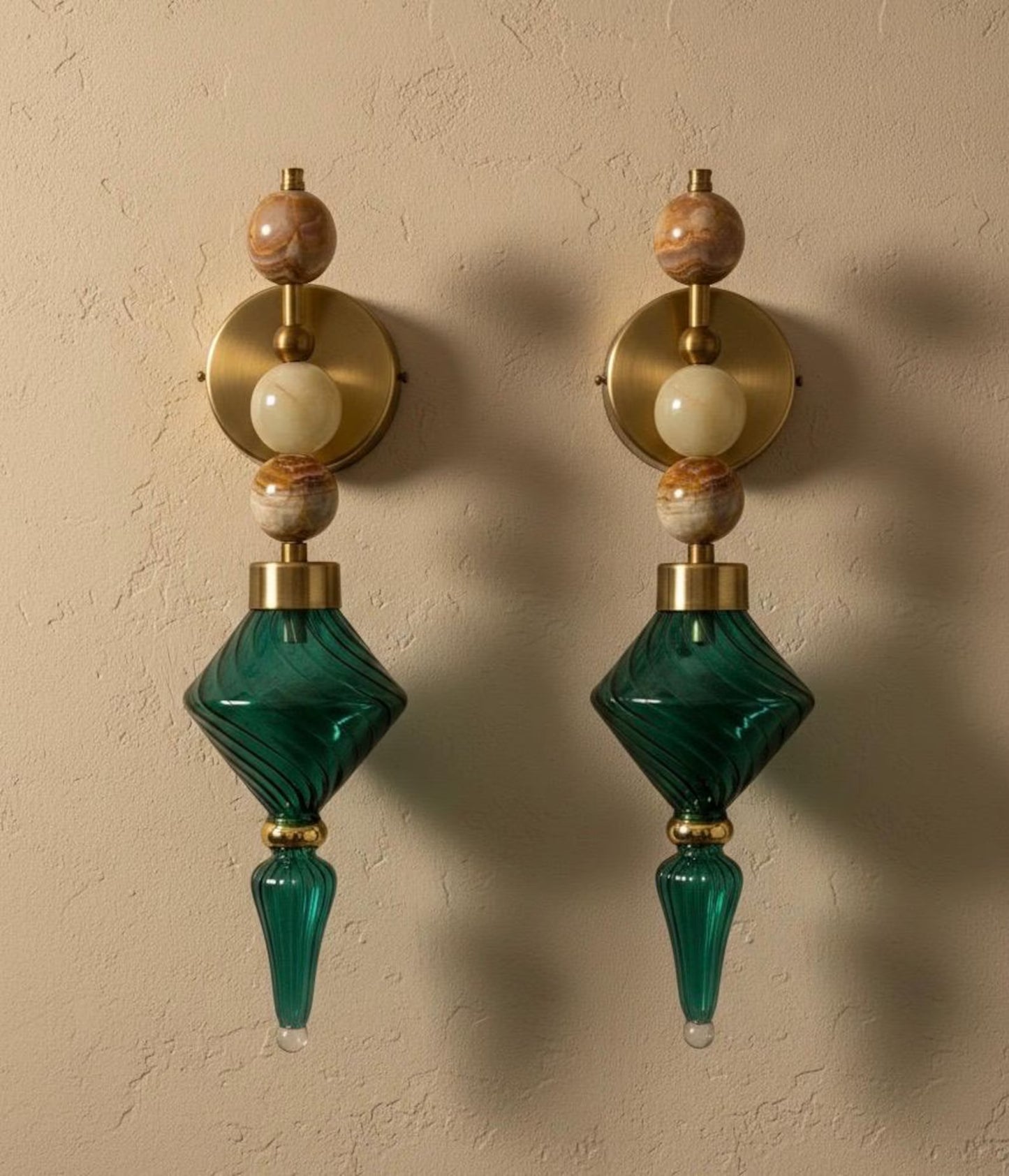 Pair of decorative wall sconces with green glass and gold accents on a beige wall.