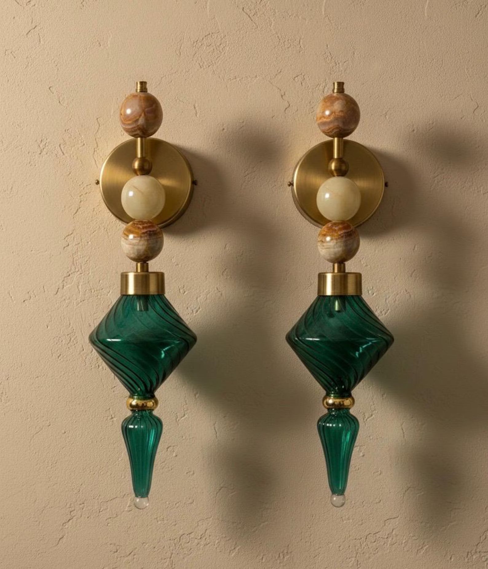 Pair of decorative wall sconces with green glass and gold accents on a beige wall.