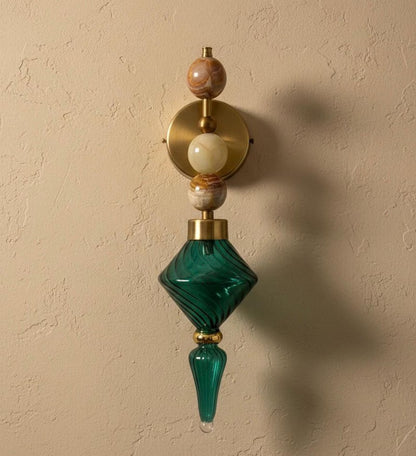 Decorative wall sconce with green glass and gold accents on a beige wall.