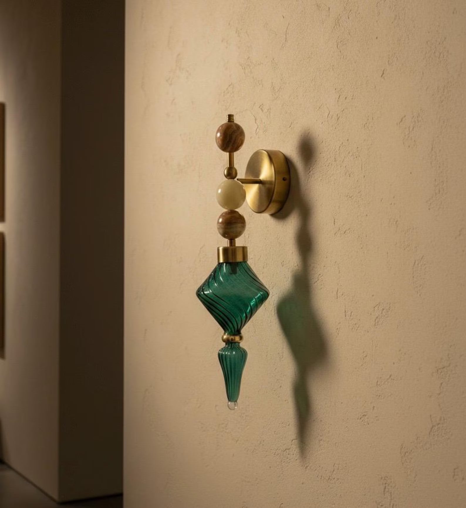 Decorative wall sconce with green glass and gold accents on a beige wall.