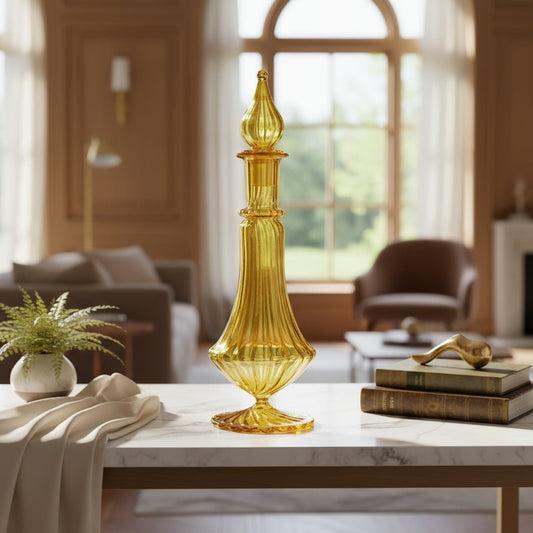 A yellow glass decanter bottle with a golden stopper and ornate design, featuring a tall, ribbed pedestal base.