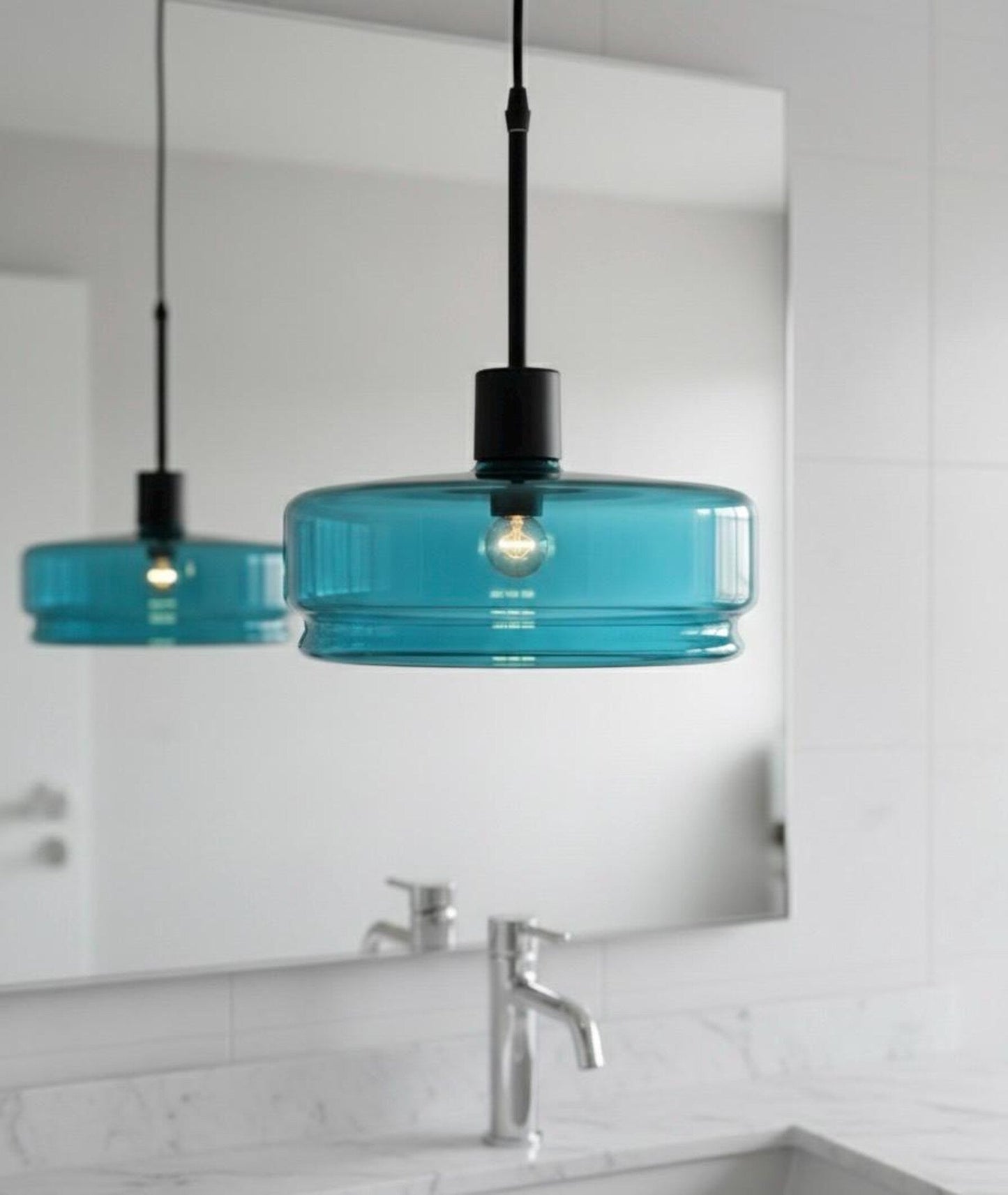 Turquoise pendant lights hanging above a bathroom vanity with a mirror.