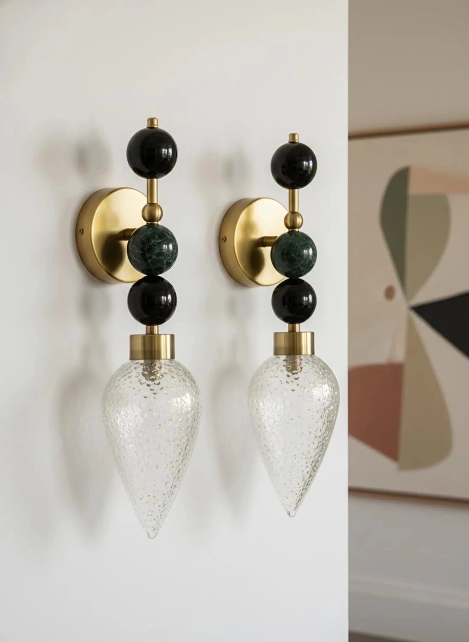 Pair of wall sconces with gold, black, and clear design on a white wall.