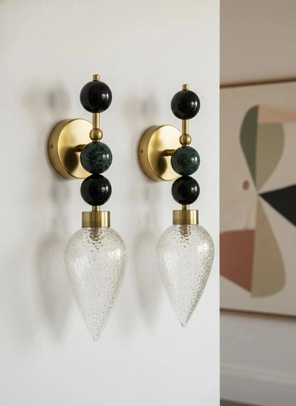 Pair of wall sconces with gold, black, and clear design on a white wall.