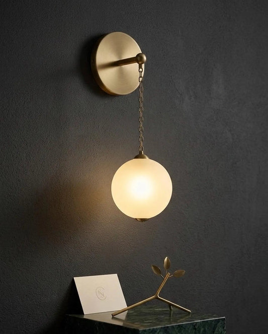 Wall-mounted lamp with a round glass shade on a dark wall.