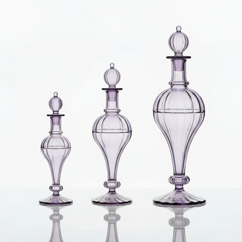 Purple glass decanter on a marble surface with lavender flowers and rings, against a light purple background | Les Trois Pyramides