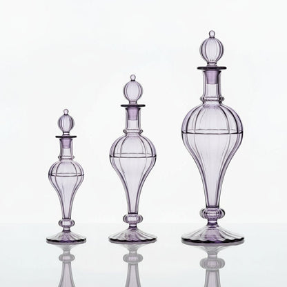 Purple glass decanter on a marble surface with lavender flowers and rings, against a light purple background | Les Trois Pyramides