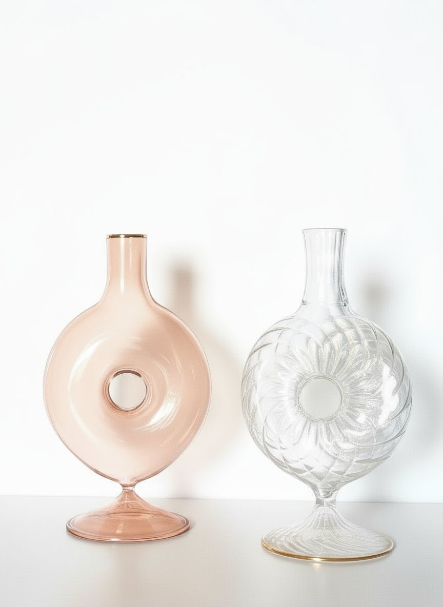 Two glass vases, one pink and one clear with floral design, on a white background