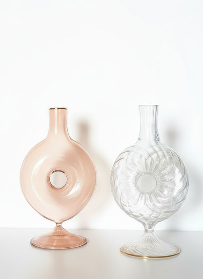 Two glass vases, one pink and one clear with floral design, on a white background