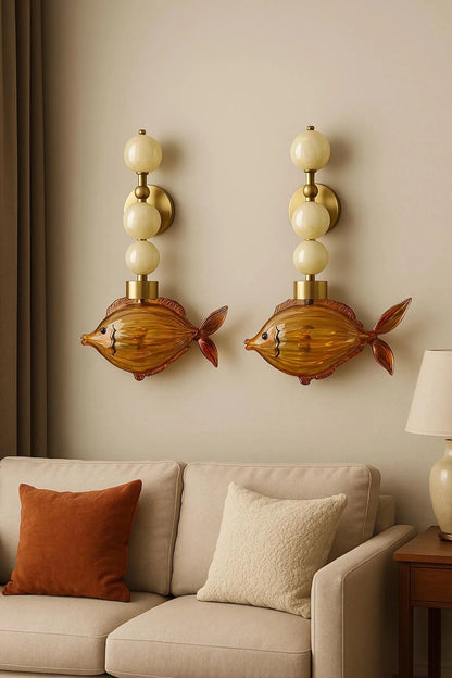 Two fish-shaped wall sconces on a beige wall above a beige sofa with decorative pillows.