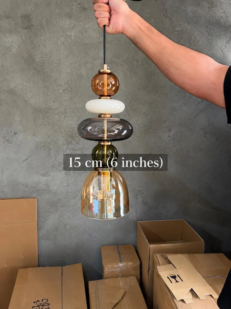 Handmade glass pendant light featuring amber, milky white, smoky grey and olive green glass elements, with brass accents and a clear champagne glass shade | Les Trois Pyramides