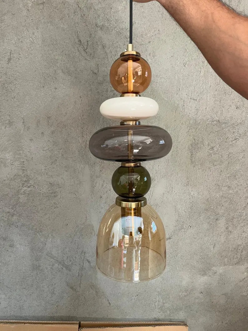 Handmade glass pendant light featuring amber, milky white, smoky grey and olive green glass elements, with brass accents and a clear champagne glass shade | Les Trois Pyramides
