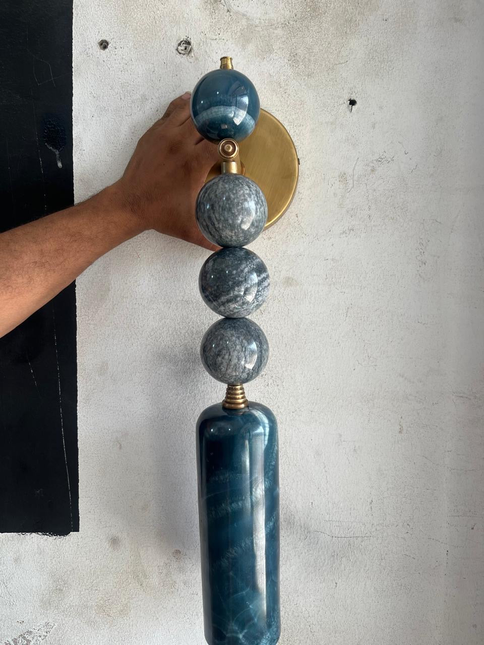 Decorative wall sconce with blue marbled design held by a hand against a light gray wall - Les Trois Pyramides